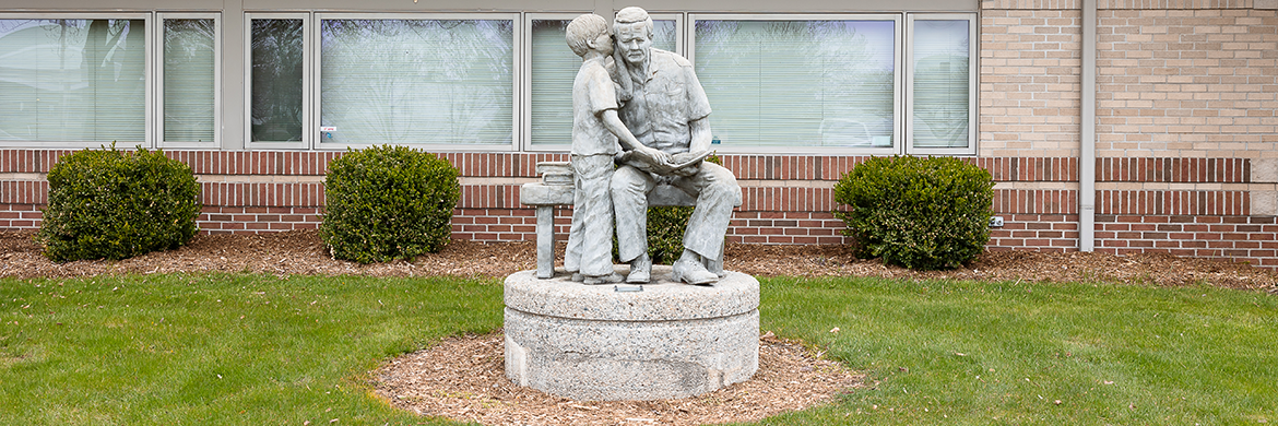 Statue in front of the library of a boy whispering in a man's ear